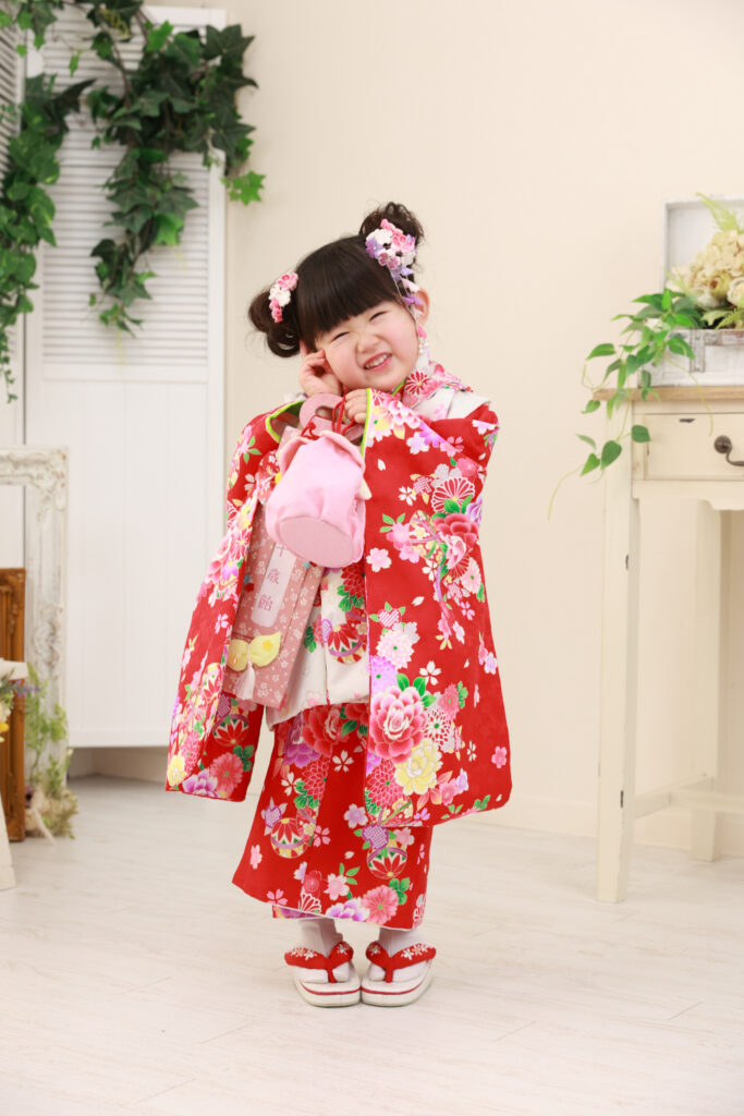 赤系の三つ身着物を着た3歳女の子の笑顔写真