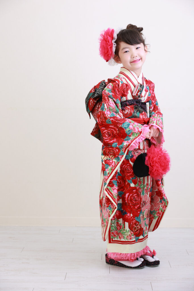 バラ柄の赤い着物に大きな髪飾りをつけた女の子の全身写真