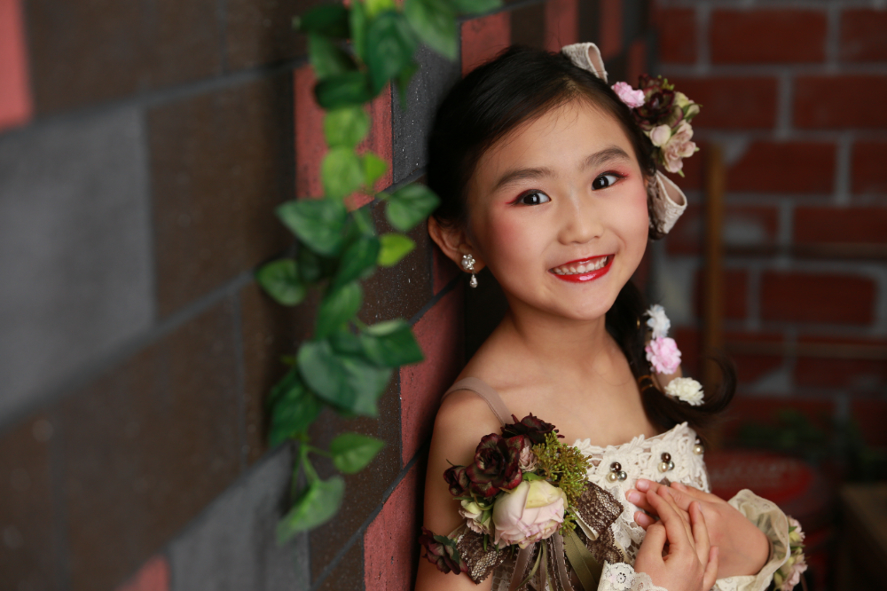れんが背景でアンティーク風ドレスを着た7歳の女の子
