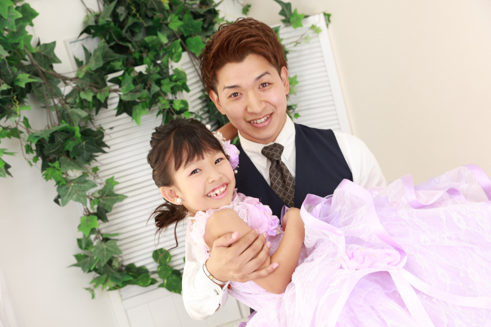 ラベンダー色のドレスを着て父に抱っこされる7歳の女の子