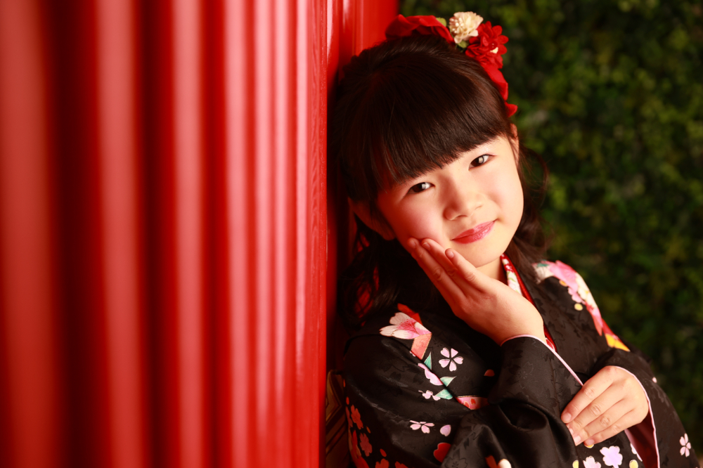 和風の壁を背景に、黒地の着物を着た7歳の女の子