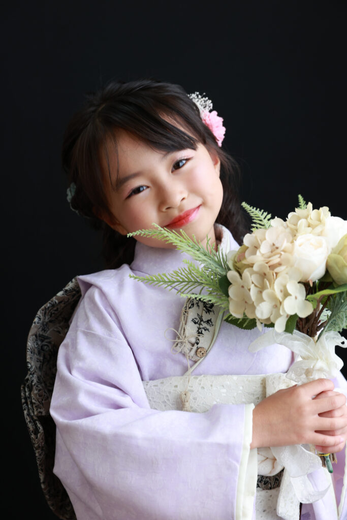 ラベンダー色の着物と黒い背景で花束を持つ7歳の女の子
