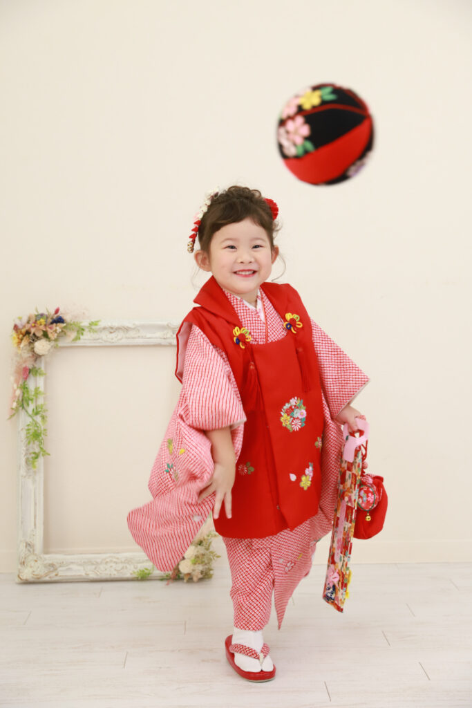 赤いまりを投げるようにポーズする3歳の女の子