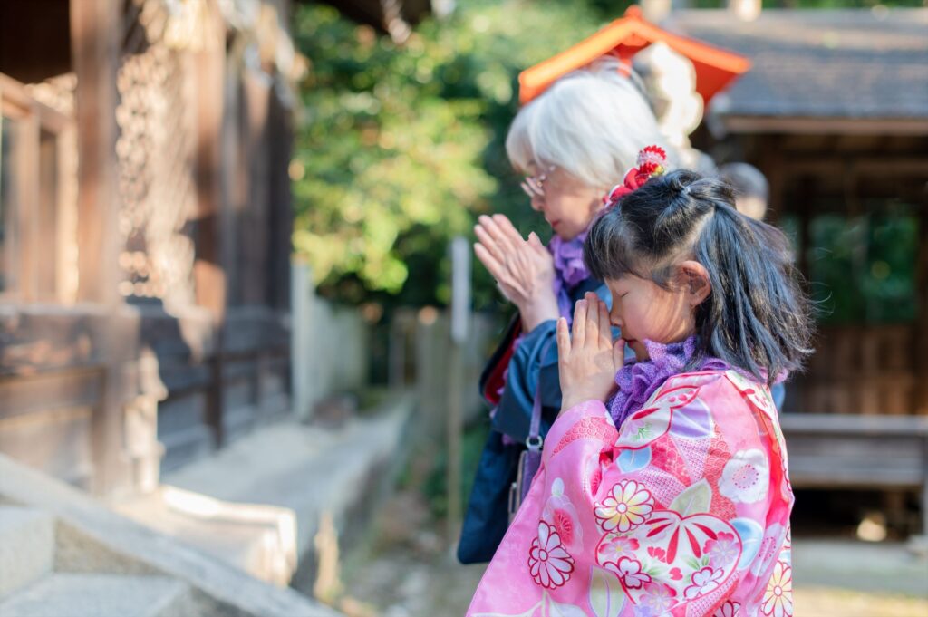 神社で手を合わせるおばあちゃんと子の写真