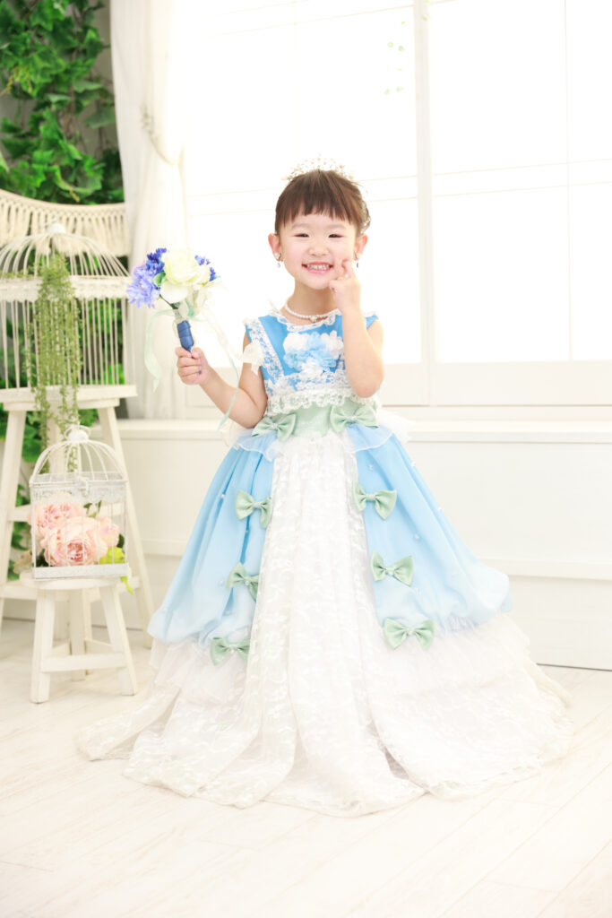 白と水色のドレスで笑顔を見せる3歳の女の子の全身写真