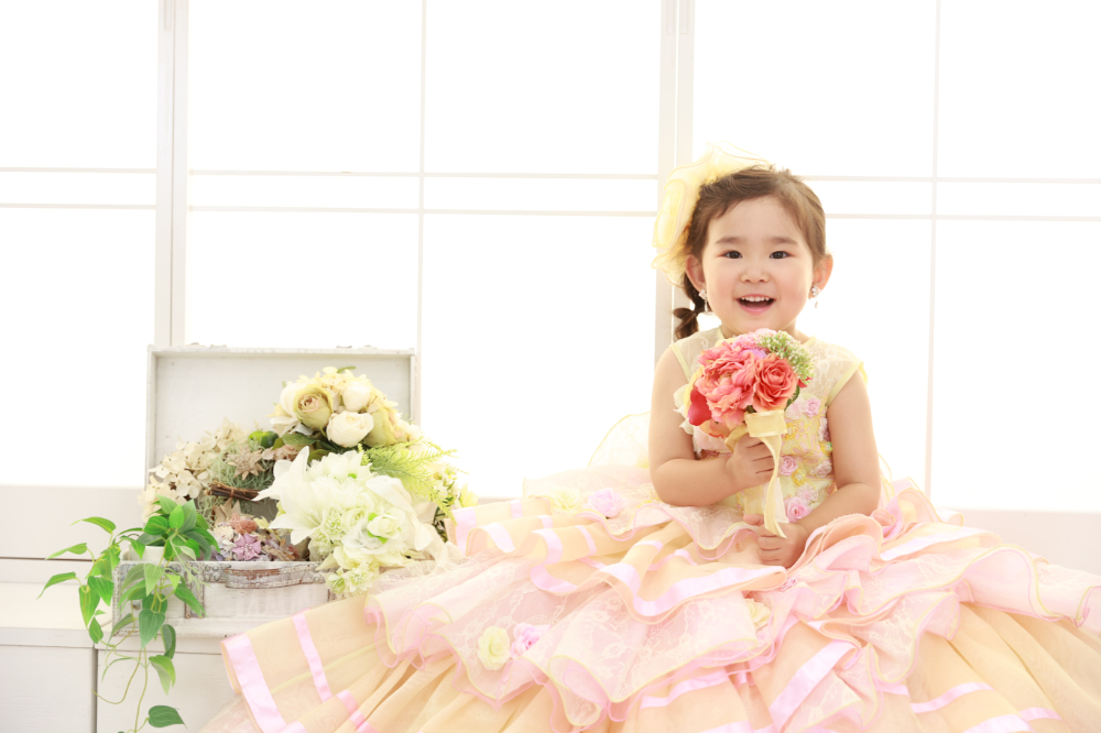 オレンジとピンクのフリルドレスでブーケを持つ3歳の女の子