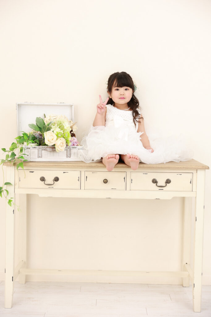 白いドレスでアンティークな机に座る3歳の女の子