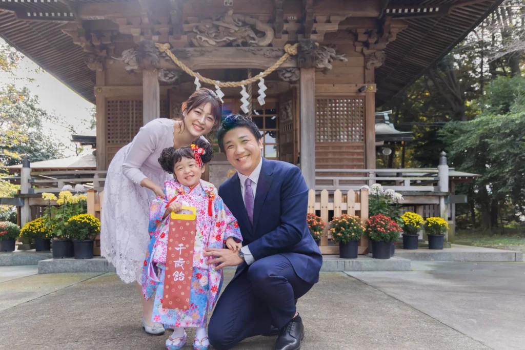 神社で七五三参りをして千歳飴を持つ親子