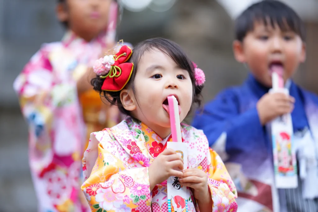 紅白の千歳飴を袋から取り出し舐める子供