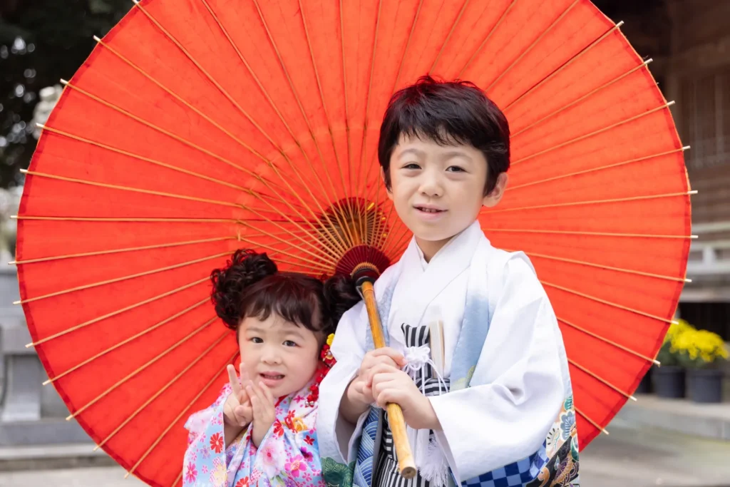 赤い和傘をさして微笑む七五三の兄妹の写真