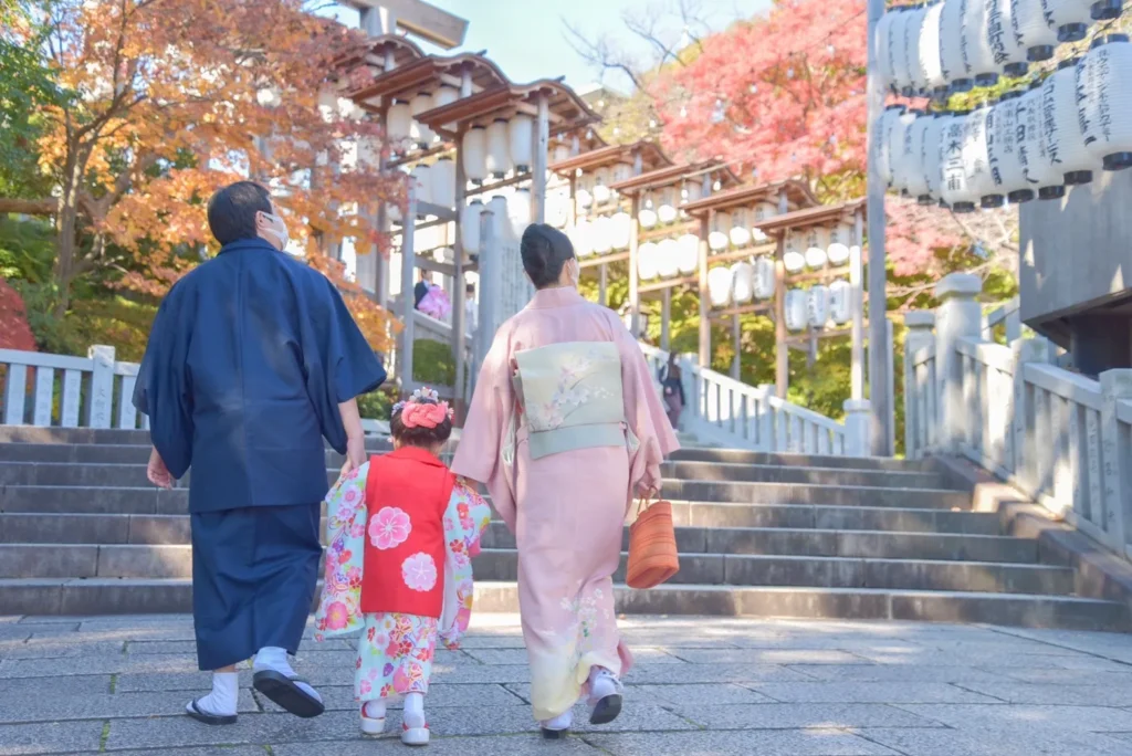 秋の紅葉が美しい神社で七五三参りをする家族