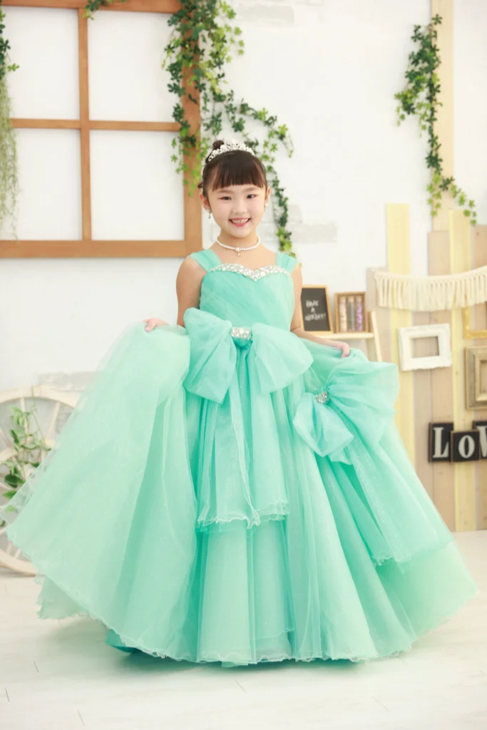 ７歳の女の子がエメラルドグリーンの大きなリボン付きドレスを着ている