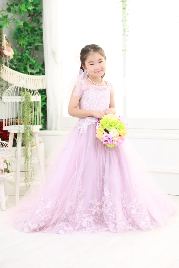 ７歳の女の子がラベンダーカラーのドレスを着て花束を持っている