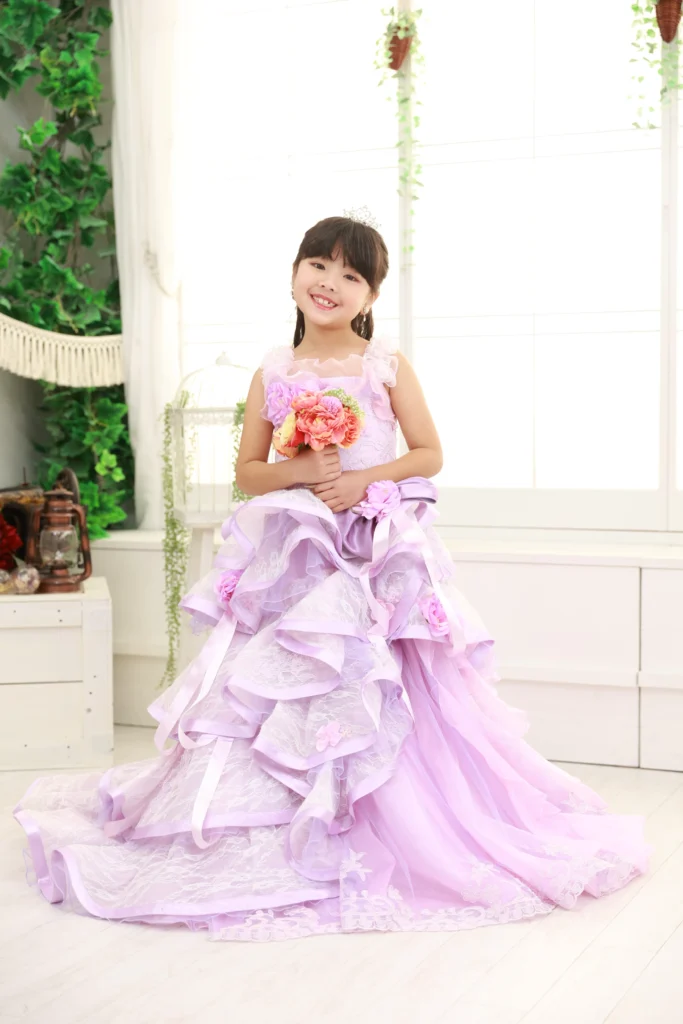 ７歳の女の子がフリルのラベンダードレスで立っている