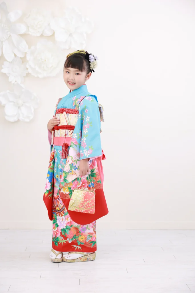 ７歳の女の子が水色と赤の古典柄着物で立っている様子