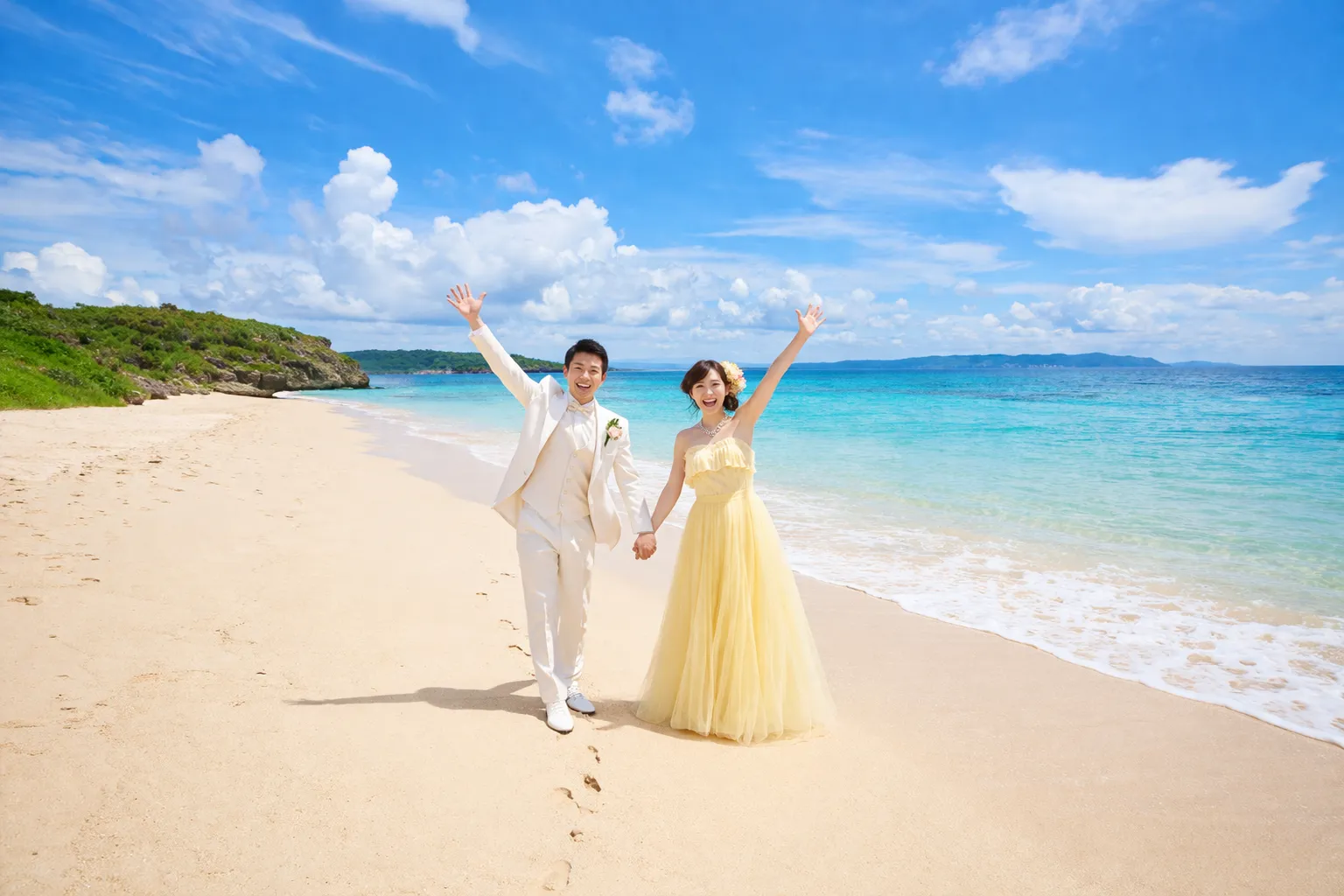 初夏のビーチで淡いイエロードレスと白タキシード姿の新郎新婦が手をつないで笑顔で手を上げている開放的なロケーションフォト