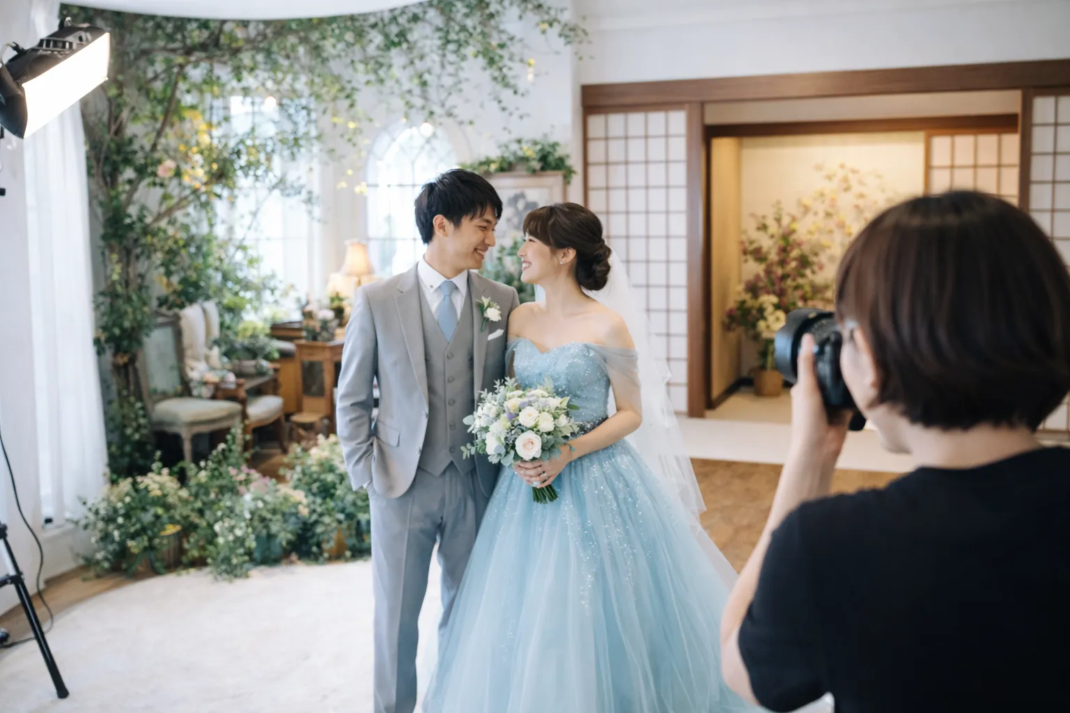 背景セットが複数あるスタジオでフォトウエディングを撮影する新郎新婦と女性カメラマン